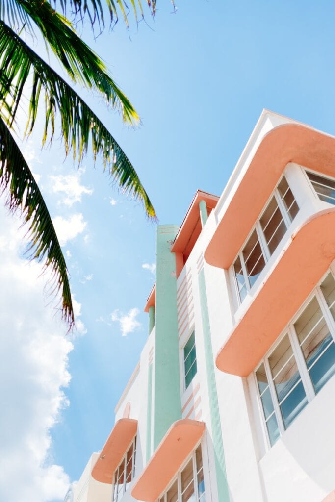 23 Top Pros and Cons of Living in Miami in 2024 3 A white two-storey building with orange window-details under palm trees during the day time. This is a beach house in Miami, a city where real estate is pricey.