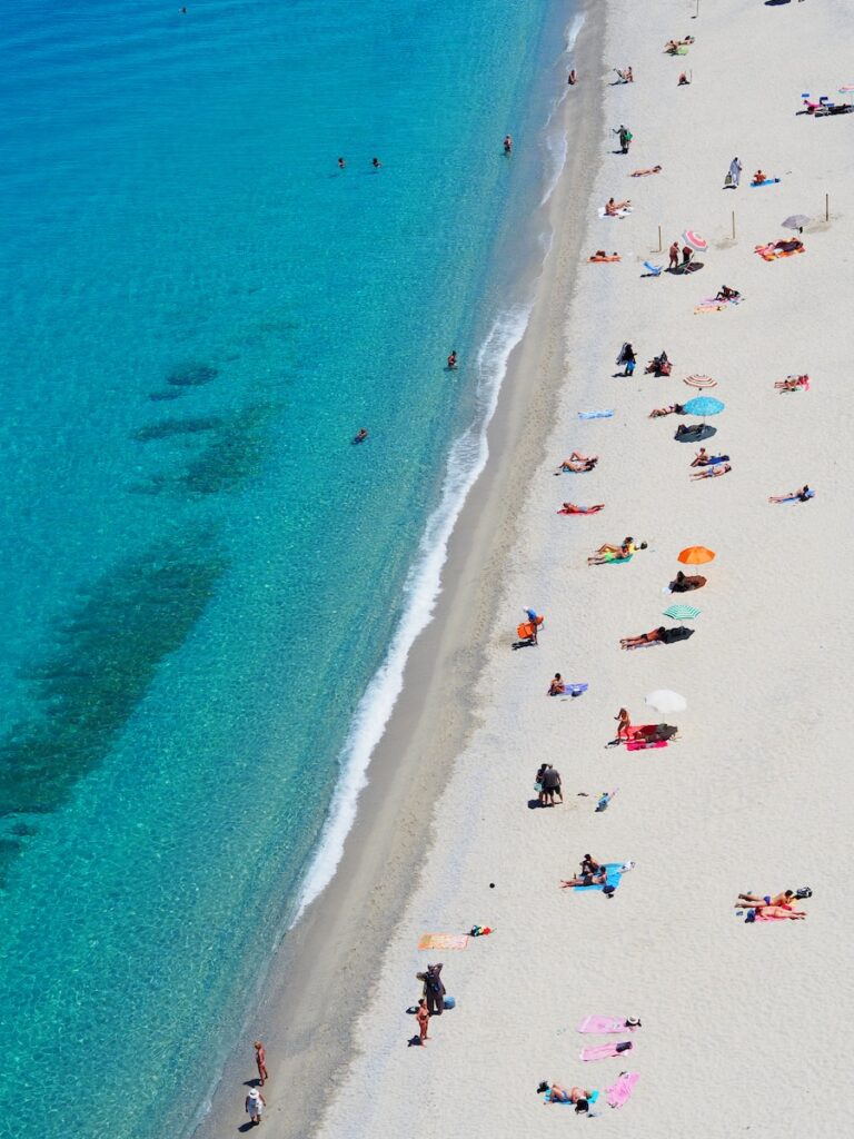 23 Top Pros and Cons of Living in Miami in 2024 8 A bird's eye view of people with their beach blankets placed on the sandy shore near a body of water. Miami's beaches are usually flocked with tourists throughout the year.