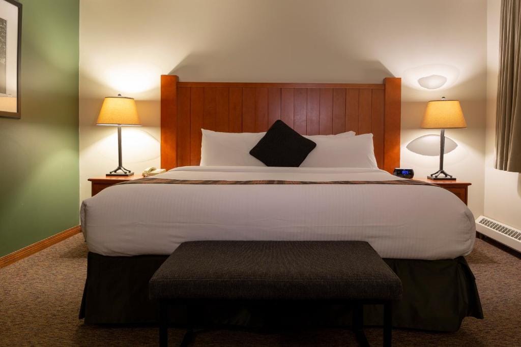 Where to Stay Near Jasper National Park: 16 Best Hotels 8 A large bed with a black ottoman in a room with white and green walls and a brown carpeted floor. Bedside tables with lamps can be seen on both sides of the bed. his comfortable room is in Whistler's Inn, one of the best hotels in Jasper National Park.