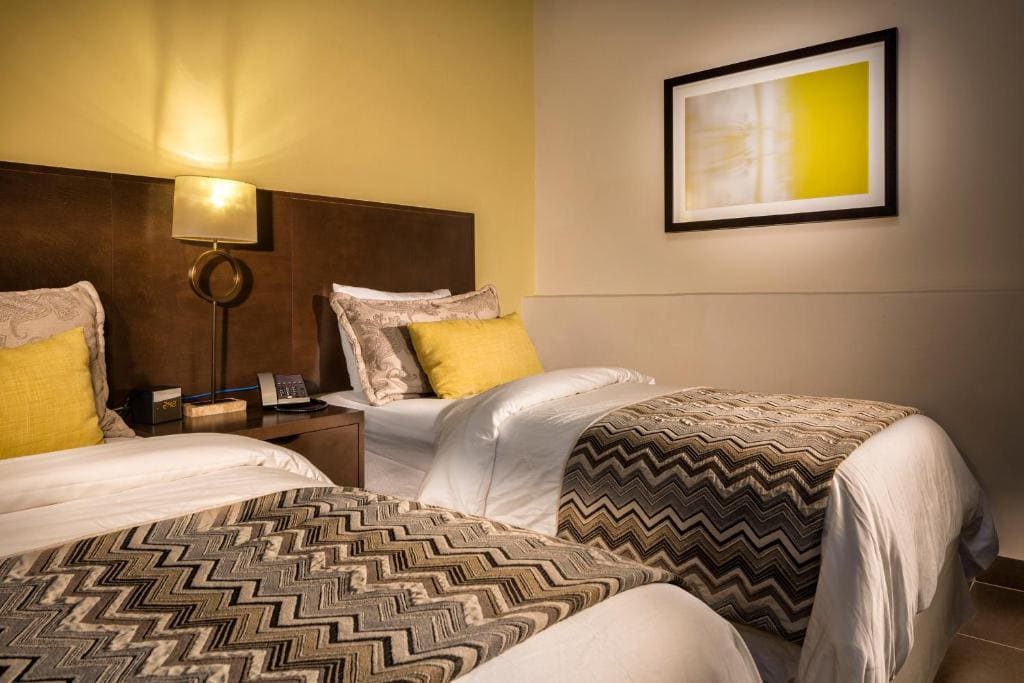 13 Best Hotels in Old San Juan, Puerto Rico 2024 10 Two single beds with white and zigzag-patterened sheets inside a beige and white colored room. A bedside table and a lamp can be seen between the beds. This is one of the rooms in the Decanter Hotel, Old San Juan.