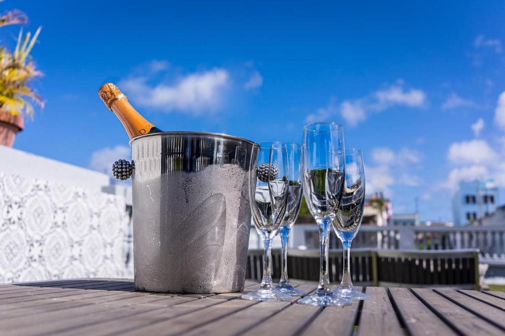 13 Best Hotels in Old San Juan, Puerto Rico 2024 16 A silver ice bucket with wine beside four gclear wine glasses placed on wooden table. The navona Studios is one of the best horels in San Juan.