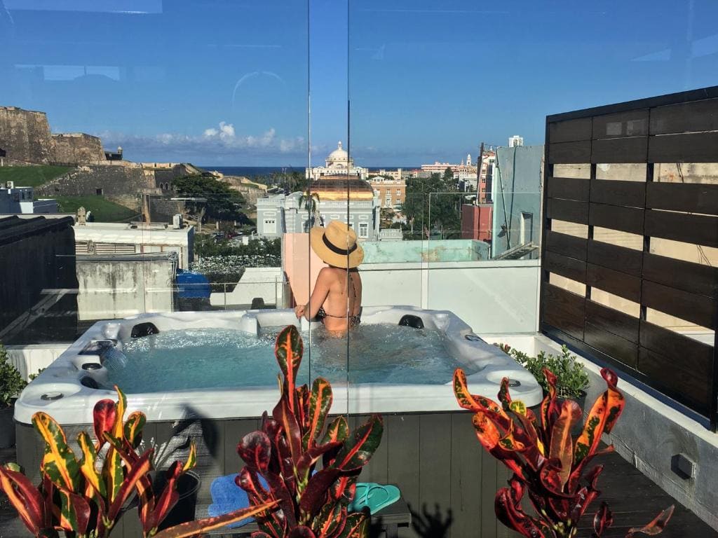 13 Best Hotels in Old San Juan, Puerto Rico 2024 2 A woman wearing a brown round hat on a hot tub on a balcony, looking at the view. This is in the 352 guest house, one of the best Old San Juan Hotels.