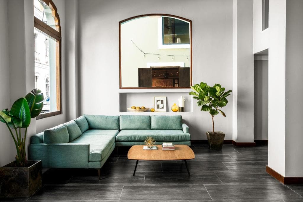 13 Best Hotels in Old San Juan, Puerto Rico 2024 3 A green L-shaped couch and a wooden coffee table. A large plant can also be seen near the window, above the couch. This is in El Colonial, one of the luxury hotels in san juan.