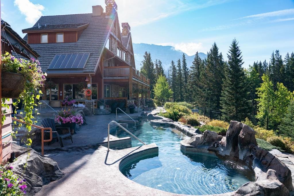 Where to Stay in Banff National Park: 18 Best Hotels (2024) 7 An outdoor swimming pool outside a two story log cabin near large green trees and a garden. his is in the Hidden Ridge Resort, one of the best options if you're wondering where to stay in Banff national Park.