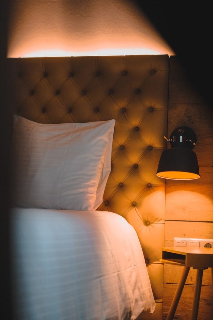 Where to Stay Near Jasper National Park: 16 Best Hotels 11 A close up photo of a bed with white sheets beside a desk and anight lamp. This is in the HI Jasper - Hostel. One of the best options if you're wondering where to stay in Jasper National Park.