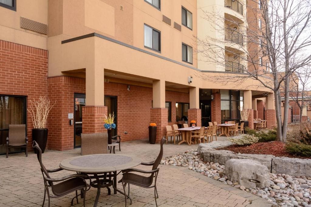 10 Best Hotels with Waterslides in Toronto 11 Three chairs with a round table on the middle near a peach colored multi storey building. This is in the Courtyard By marriott Toronto Brampton, one of the hotels with waterslides in Toronto.