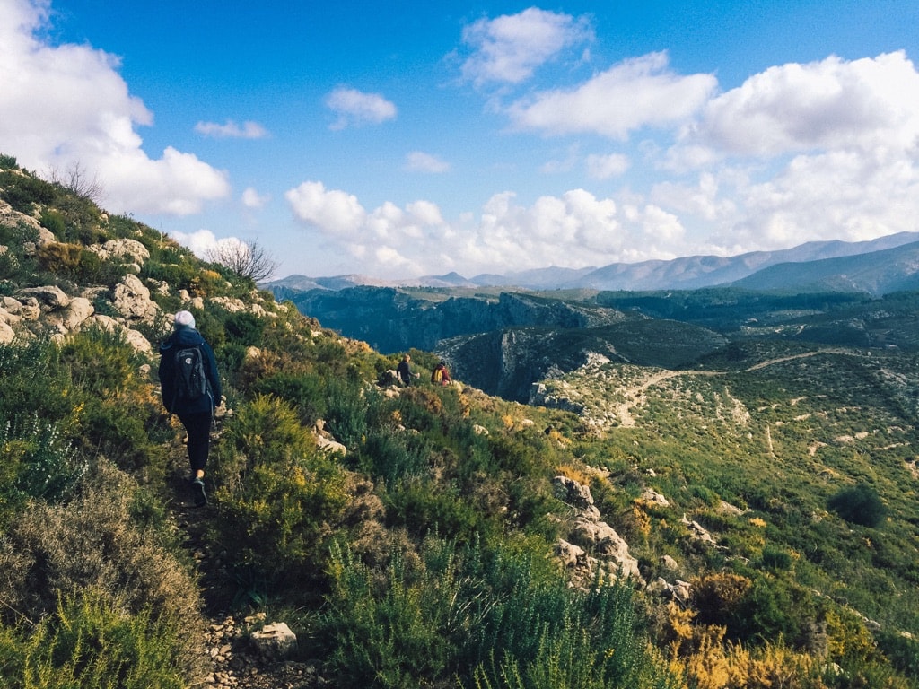 27 Pros and Cons of Living in Spain in 2024 1 Nina hiking in Benisiva Spain, where she lived. It's a mountain range with rock boulders and brush that you hike between. The mountains stretch as far as you can see