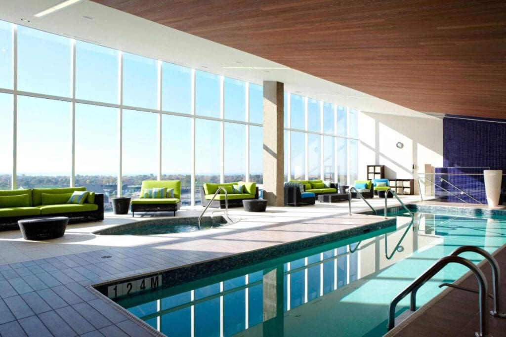 22 Best Places to Stay in Montreal Canada 23 An indoor rectangular shaped swimming pool with several green chairs near it. Large windows can also be seen in the photo with an awesome view of the city.