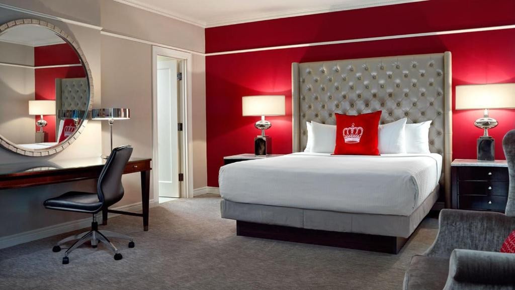 Where To Stay In Toronto: Best Areas And Hotels in 2024 5 A huge bed with a wide upholstered headboard placed in the middle of a carpeted room. A swivel chair and a large wall-mounted, circular mirror can be seen by the end of the bed. This is in the Omni King Edward Hotel in Toronto.