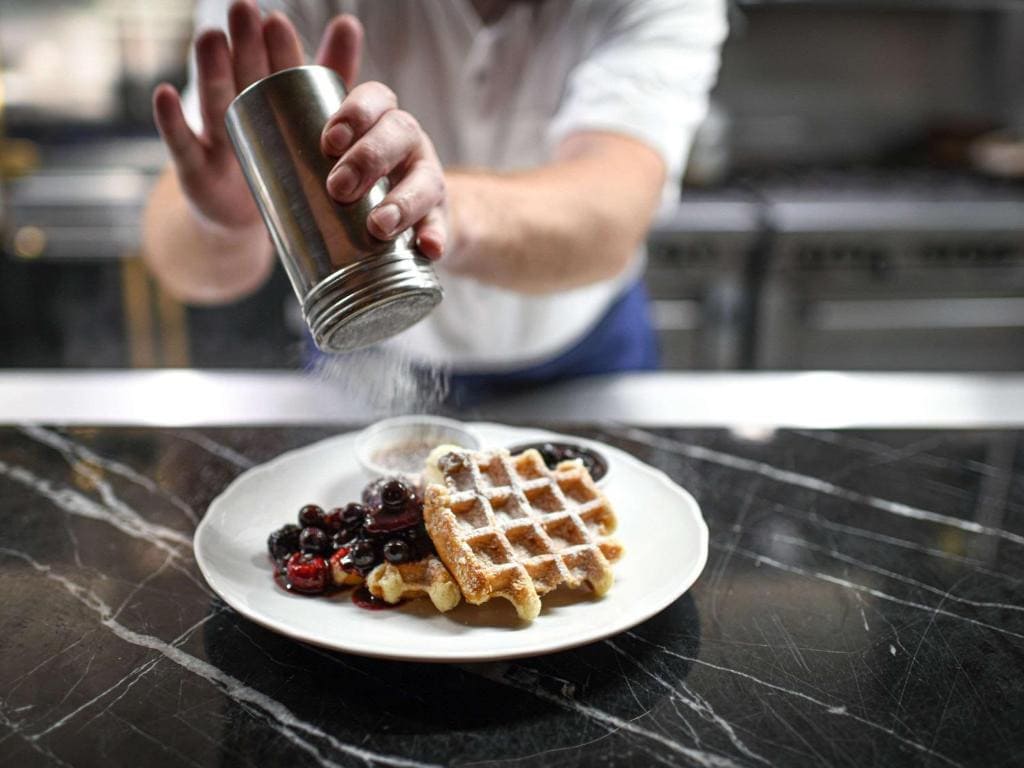 Where To Stay In Toronto: Best Areas And Hotels in 2024 6 A chef pouring powdered sugar on a dish of waffles and berries. Get a taste of amazing and tasty food in Fairmont Royal York Hotel in Toronto.