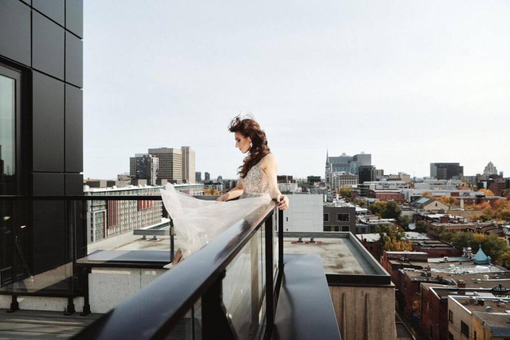 22 Best Places to Stay in Montreal Canada 21 A woman leaning on the glass fence of a balcony with a view of buildings and houses in the city. This is in the hotel St. Thomas in Montreal Canada.