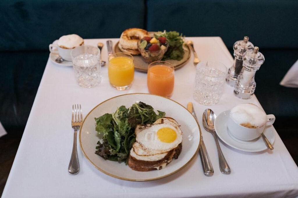 22 Best Places to Stay in Montreal Canada 1 A breakfast plate of eggs and lettuce, utensils, salt and pepper shakers, 2 glasses of juice, and 2 glasses of water on top of a white table. The Hotel Birks in Montreal Canada is one of the best places to stay in the city.