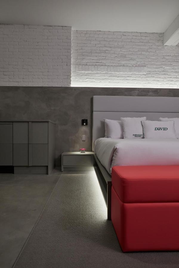 22 Best Places to Stay in Montreal Canada 10 A bed with white sheets and red ottoman inside a room with cement flooring and brick walls. A bedside cabinet with a lamp can be seen beside the bed. This is in David hotel, one of the best places to stay in Montreal Canada.