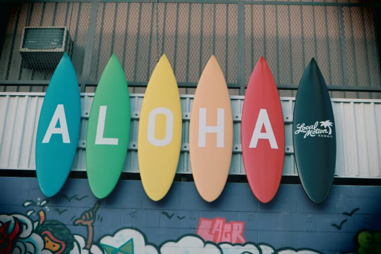You’re Welcome in Hawaiian & 21 Common Phrases 1 Aloha written on multi coloured surf boards hung on the side of a building