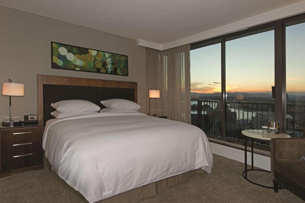 21 Best Places To Stay In Victoria, Canada 2024 7 A large bed with white sheets inside a room with carpeted flooring and beside a large sliding door towards a balcony offering a view of the city. This is in Double Tree Hotel, one of the best places to stay in Victoria, Canada.