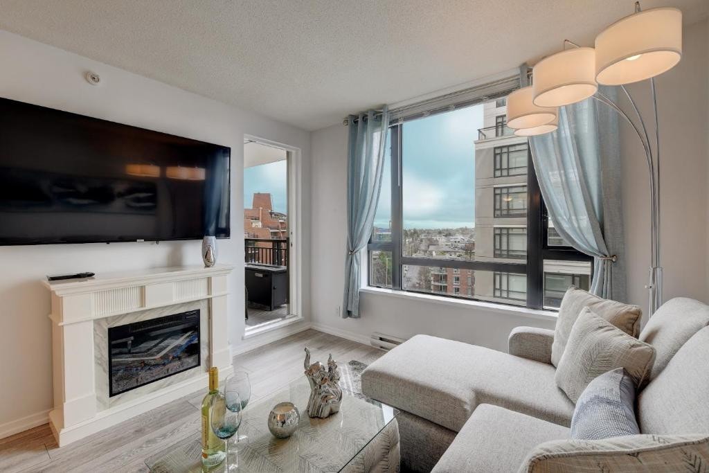 21 Best Places To Stay In Victoria, Canada 2024 9 A living room with white couches and a wall mounted TV un front of it and above a fireplace. A door towards a balcony can also be seen beside the TV, this is in the Astoria Flair in Victoria.