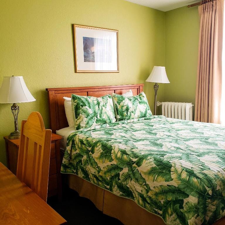 21 Best Places To Stay In Victoria, Canada 2024 11 A bed with tropical leaves printed sheets inside a room with green walls and two bedside tables and lamps. This is in the James Bay Inn Hotel in Victoria.