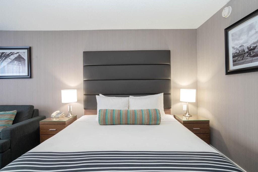 11 Best Edmonton Hotels With Balconies 2024 7 A bed with plain white and striped sheets and upholstered headboard. Two bedside tables and lamps are placed on each side of the bed. This is in the Sandman hotel Edmonton West.