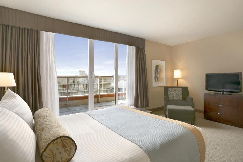 21 Best Places To Stay In Victoria, Canada 2024 12 A room with a large bed in front of a TV on top of a dresser beside a green single sofa. A sliding door that leads to a balcony is beside the bed.