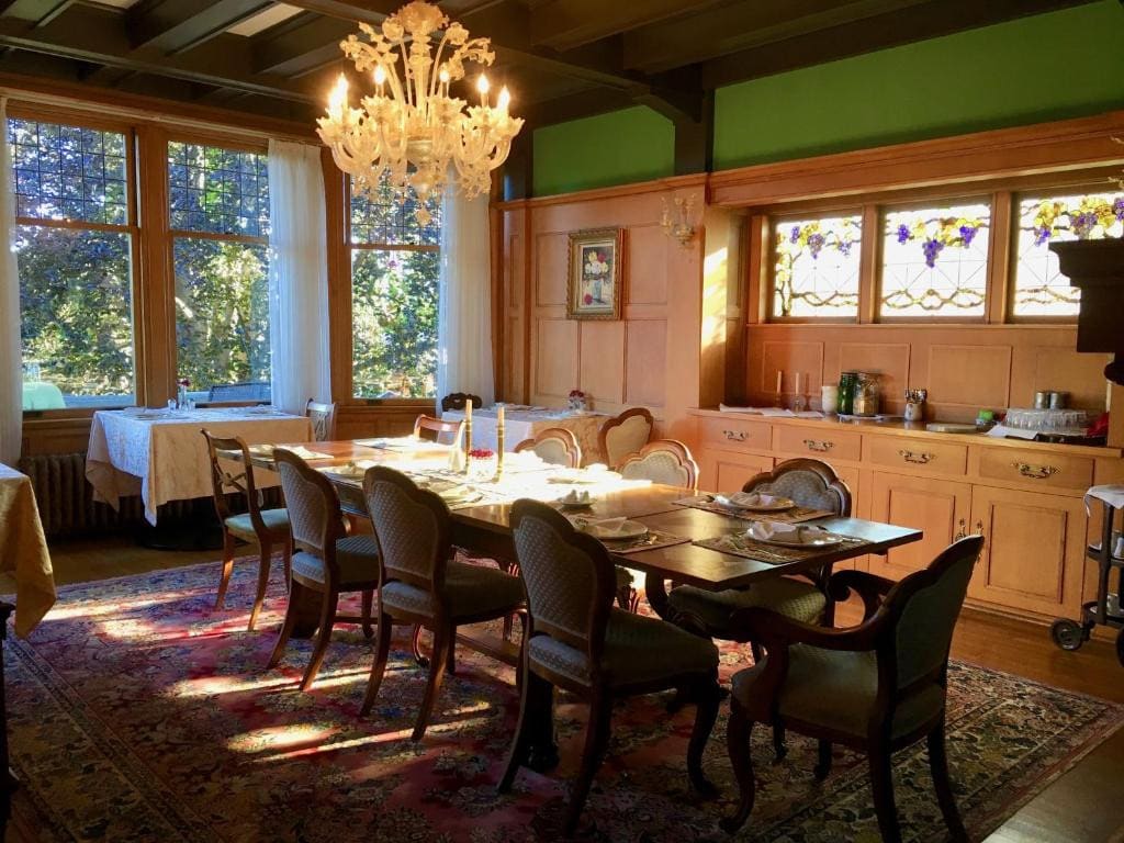 21 Best Places To Stay In Victoria, Canada 2024 15 A dining table with 7 chairs in a dining room with a large rectabgular carpet, wooden counters, and windows. This is in the Prior Castle Inn in Victoria Canada.