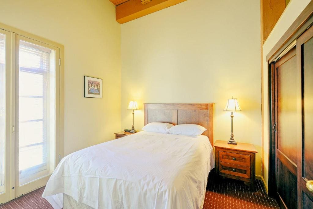 21 Best Places To Stay In Victoria, Canada 2024 17 A bed with white sheets inside a room with wooden dressers and two bedside tables and lamps. A large window can be seen beside the bed. This is in the Swans Brewery in Victoria, Canada.