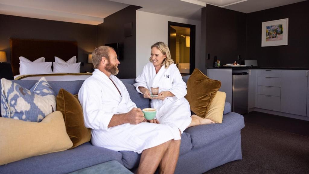 18 Best Hotels in Christchurch, New Zealand 2024 4 Two people in white robes sitting in a blue couch holding cups of coffee and talking to each other. This is a hotel room in Hotel montreal in Christchurch.