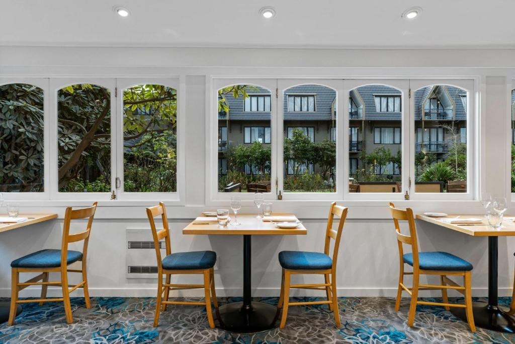 18 Best Hotels in Christchurch, New Zealand 2024 8 Several sets of tables and chairs near a large windows inside a floral carpeted room. Chateau on the park is one of thest places to stay in Christchurch.