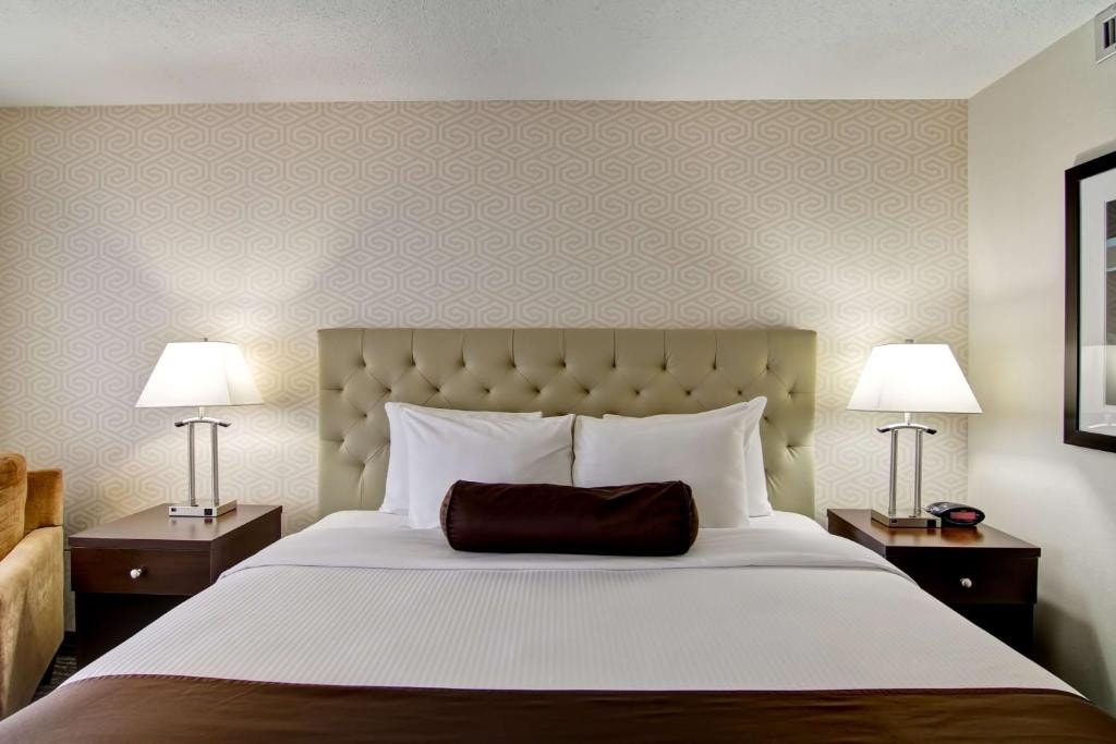 11 Best Edmonton Hotels With Balconies 2024 9 A large bed with white and brown sheets and pillows and an upholstered headboard. Bedside tables and lamps are placed on both sides of the bed. This is The Best Western Cedar Park Inn in Edmonton.