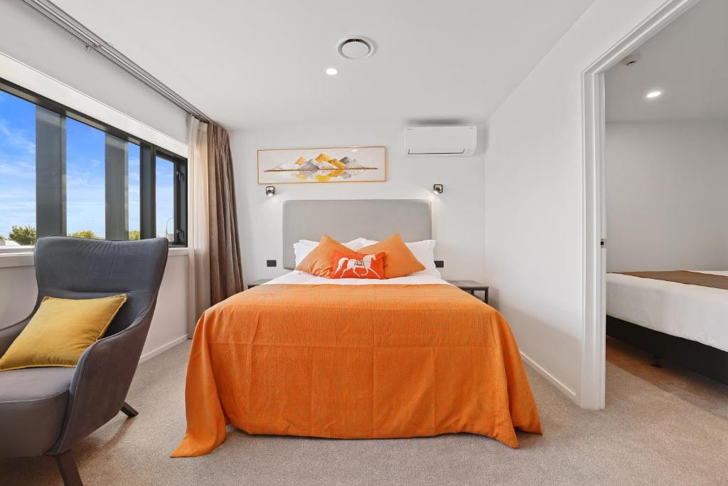 18 Best Hotels in Christchurch, New Zealand 2024 10 An orange bed inside a room with airconditioner, a grey chair, and a large window. This is in the Golden Hotel.