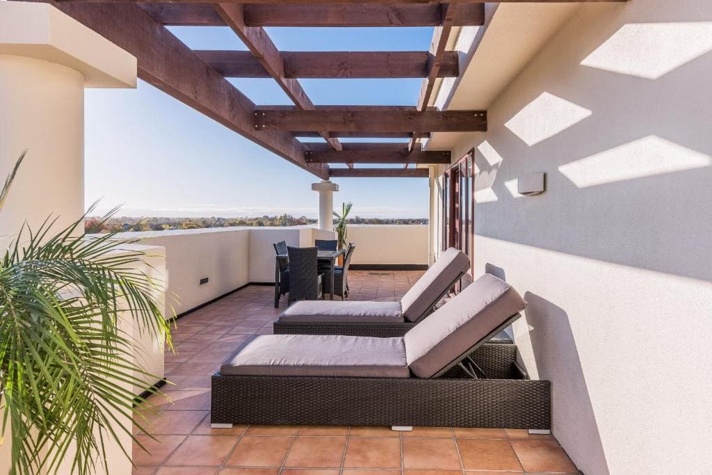 18 Best Hotels in Christchurch, New Zealand 2024 11 a couple of sunbeds on the roof of Fino Hotel & Suites. There's a view of the city along with greenery and a table & chairs.
