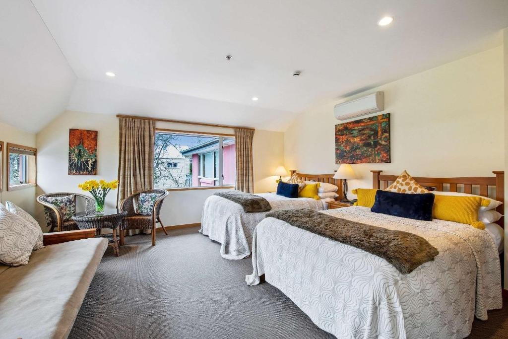 18 Best Hotels in Christchurch, New Zealand 2024 12 Two large beds facing a couch inside a carpeted room. Two chairs and a circular table can be seen near a window beside one bed. The Classic villa is one of the best places to stay in Christchurch.