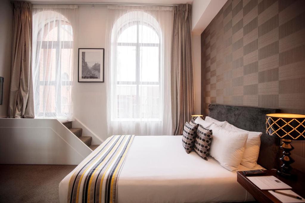 18 Best Hotels in Christchurch, New Zealand 2024 14 A bed inside a carpeted room with a small stairway leading to a large window. This is in Hotel 115 in Christchurch, New Zealand.