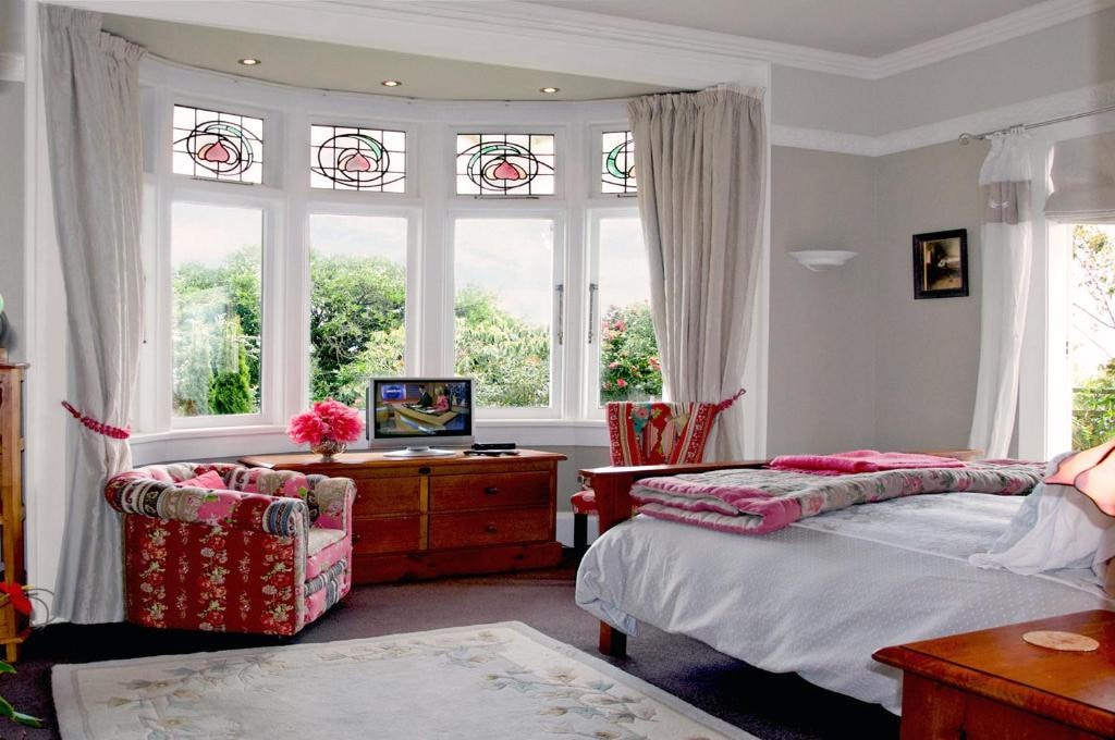 18 Best Hotels in Christchurch, New Zealand 2024 16 A bed fasing a TV on top of a dresser and a red chair beside it. This is in the Dyers House in Christchurch New Zealand.