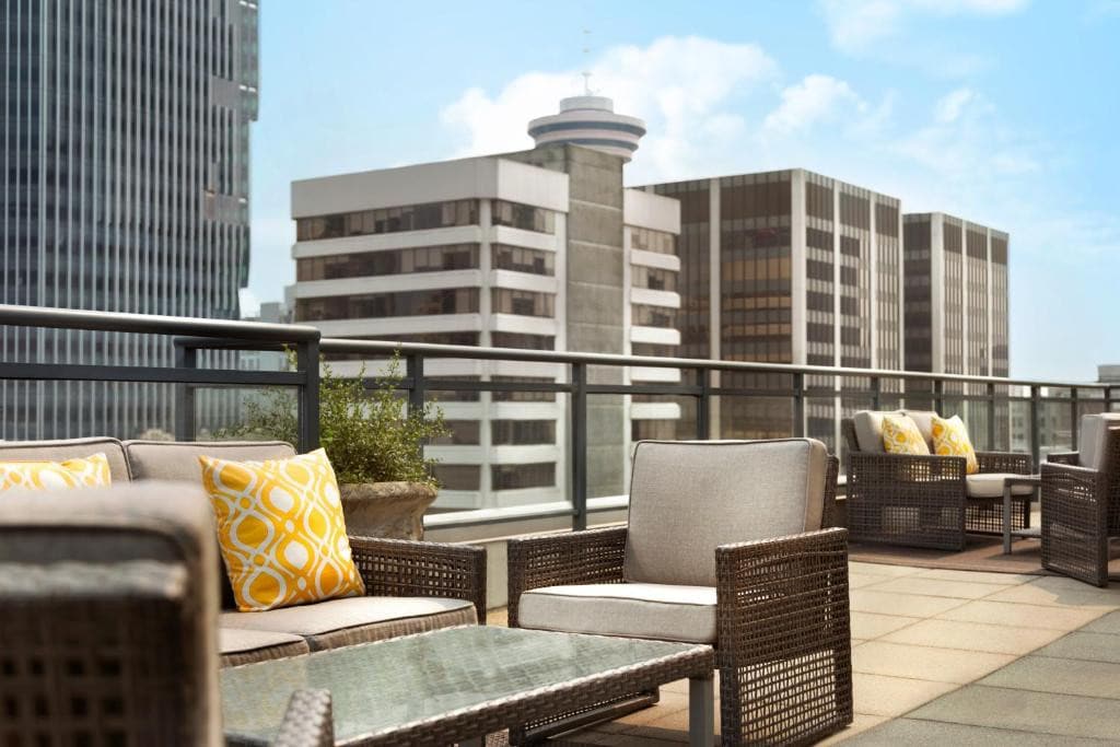 A balconi with tiled flooring and a rattan couch set. The railings ae made of metal and glass and it offers an amazing view of tall buildings. This is in Hotel Le Soleil in vancouver.