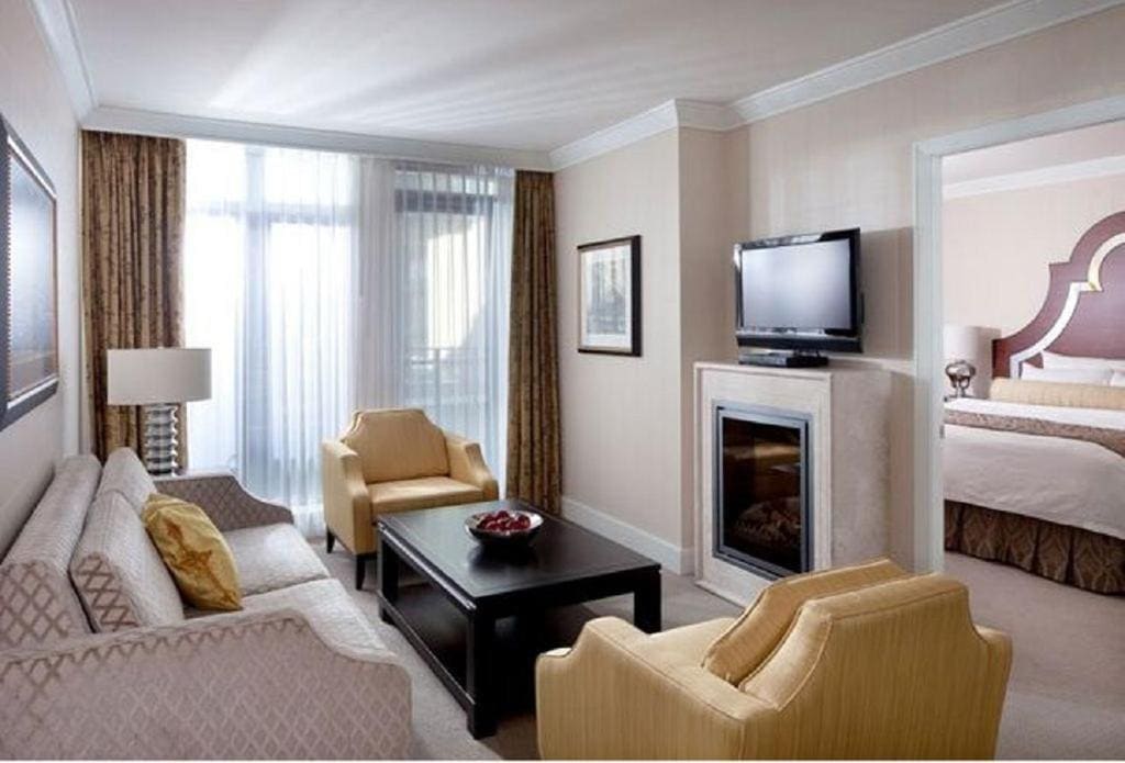 23 Best Vancouver Hotels with Balconies (A Local’s Guide) 3 A living room with a sofa, two yellow chairs, a coffee table, a TV, and a firplace. A sliding door towards a balcony can also be seen near one of the chairs. This is in the L'Hermitage in Vancouver.