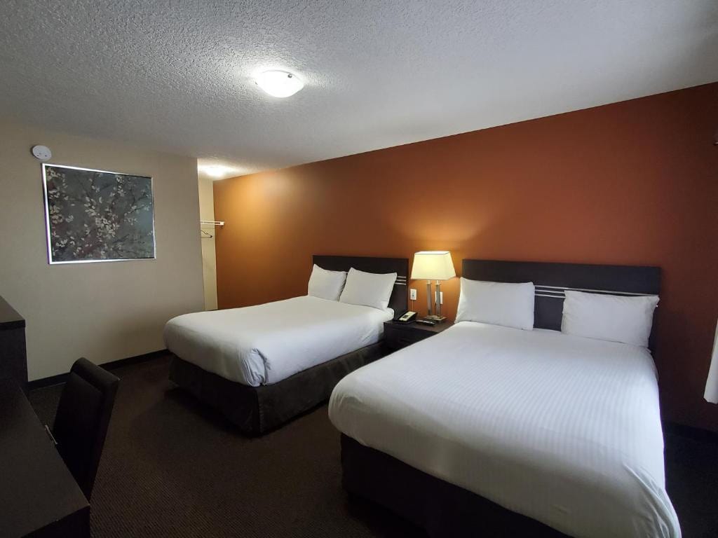 11 Best Edmonton Hotels With Balconies 2024 11 Two twin beds with white sheets inside a carpeted room. A wooden table and a swivel chair is placed in front of the beds. This is in the Royal Lodge in South Edmonton, one of the best hotels with balconies in Edmonton.