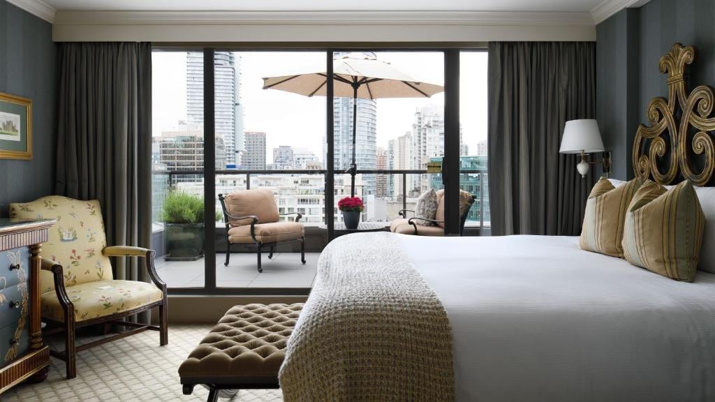 23 Best Vancouver Hotels with Balconies (A Local’s Guide) 15 A large bed inside a room and an ottoman on its end. A sliding door towards abalcony wth chairs and a table with parasol can be seen beside the bed. This is in Wedgewood Hote & Spa.
