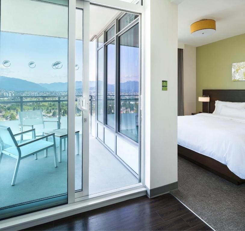 23 Best Vancouver Hotels with Balconies (A Local’s Guide) 16 A door towards a balcony with two chairs and a small square table near a bed inside a carpeted room. This is in Element Vancouver.