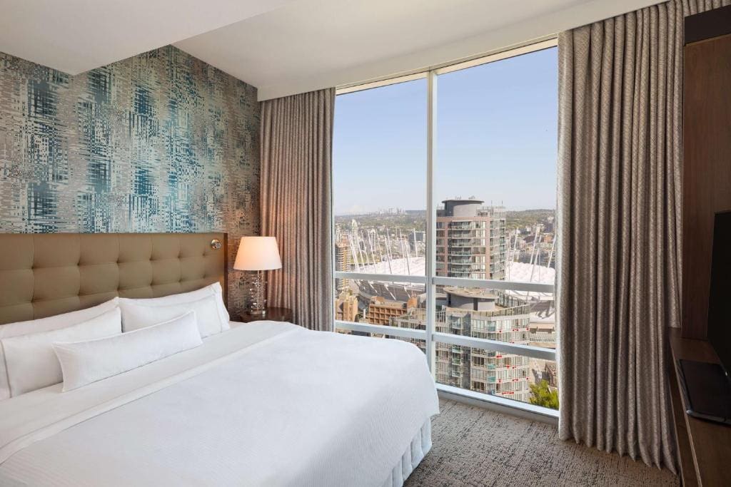 23 Best Vancouver Hotels with Balconies (A Local’s Guide) 19 A large bed inside a carpeted room beside a large window hat offers a stunning view of the city. This is in Hilton Vancouver Downtown.