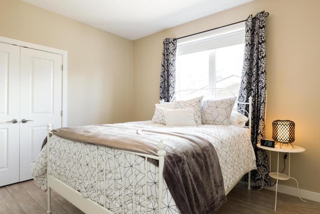 11 Best Edmonton Hotels With Balconies 2024 12 A large, cozy bed inside a room with wooden flooring. A huge window is placed above the headboard and a two-door closet is found beside the bed. This is in the EXECUTIVE YEG Home in Edmonton.