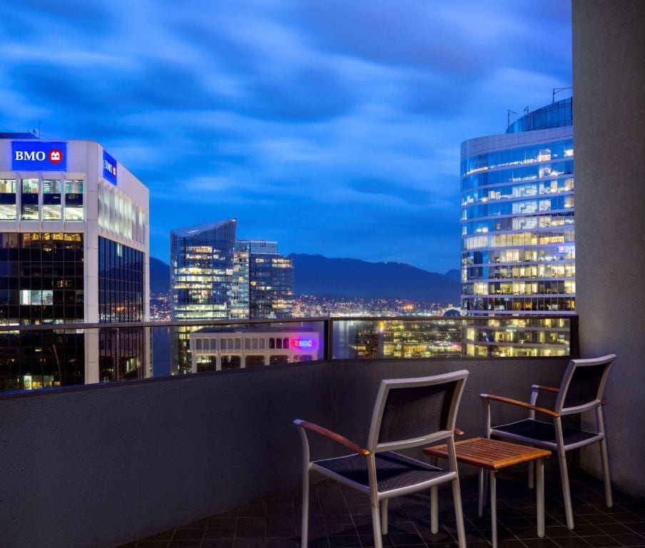 23 Best Vancouver Hotels with Balconies (A Local’s Guide) 20 Two chairs on a balcony with cement and metal railings, offering a view of the city dring night time. This is in Hyatt Regency Vancouver.