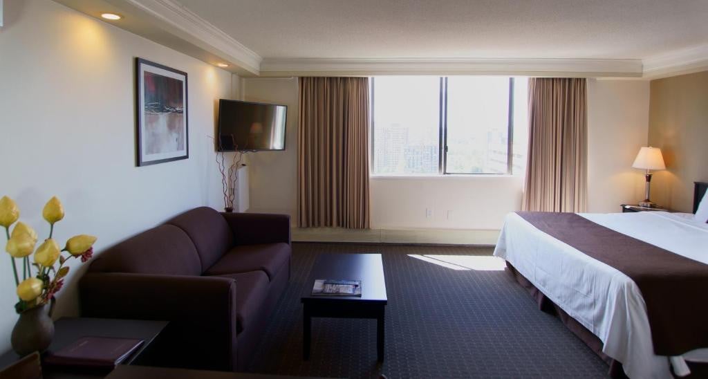 23 Best Vancouver Hotels with Balconies (A Local’s Guide) 23 A brown couch and a coffee table in front of a bed. A sliding window can be seen beside the bed. This is in the Century Plaza hotel, vancouver.