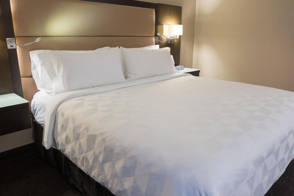 23 Best Vancouver Hotels with Balconies (A Local’s Guide) 26 A large white bed with an upholstered headboard inside a carpeted room. This is in the Holiday Inn Vancouver Downtown