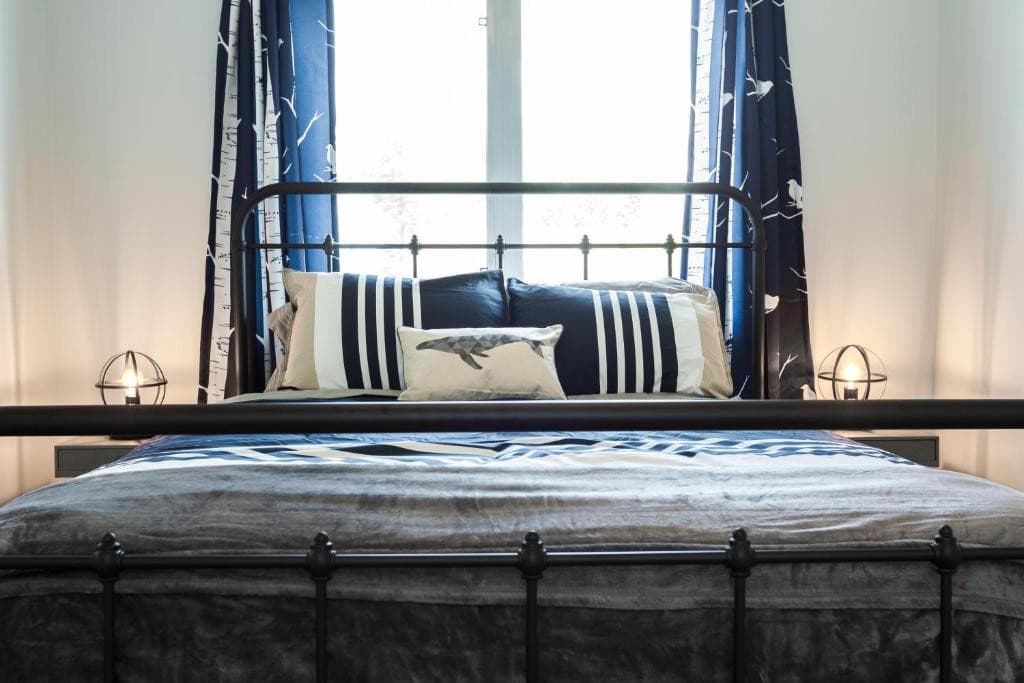 11 Best Edmonton Hotels With Balconies 2024 14 A bed with striped sheets and pillows inside a room. A window can be seen above the headboard. This is in the Mountain Style Home, one of the best Edmonton Hotels with Balconies