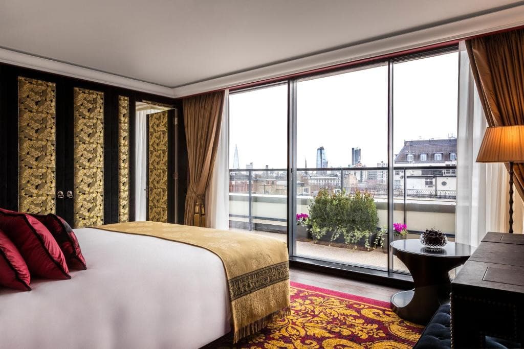 27 Best London Hotels with Balconies 2024 5 A hotel room with a large bed and gold and brown curtains. In front of the bed is a balcony overlooking a stunning view. This is in the L'Oscar London.