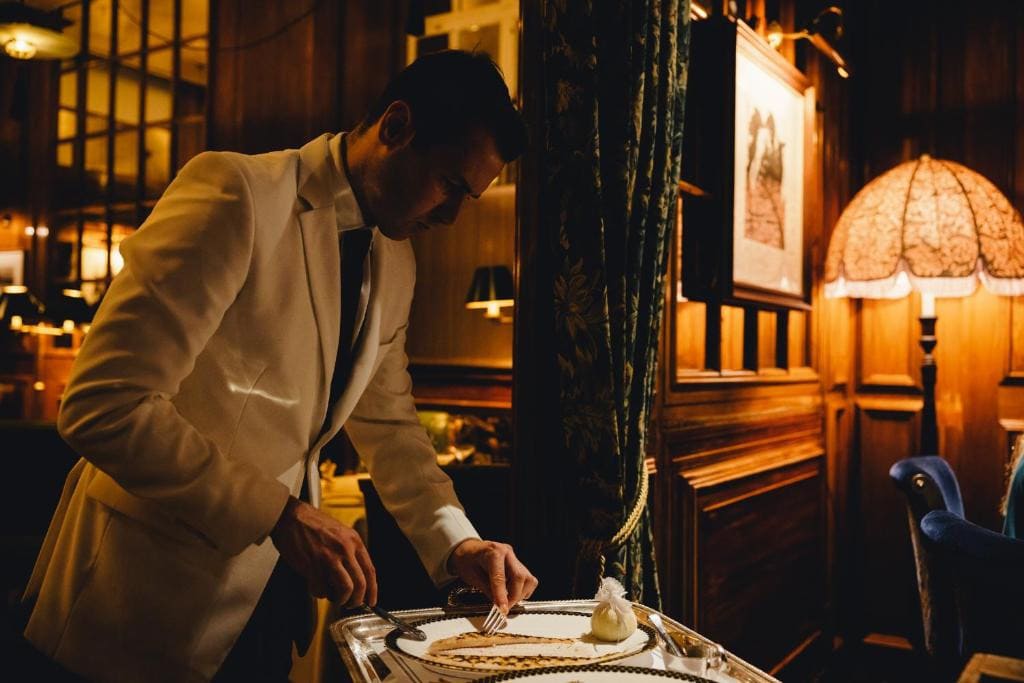 27 Best London Hotels with Balconies 2024 8 A man in a white suit preparing food in a restaurant. This is in The Ned, one of the best london hotels with balconies.