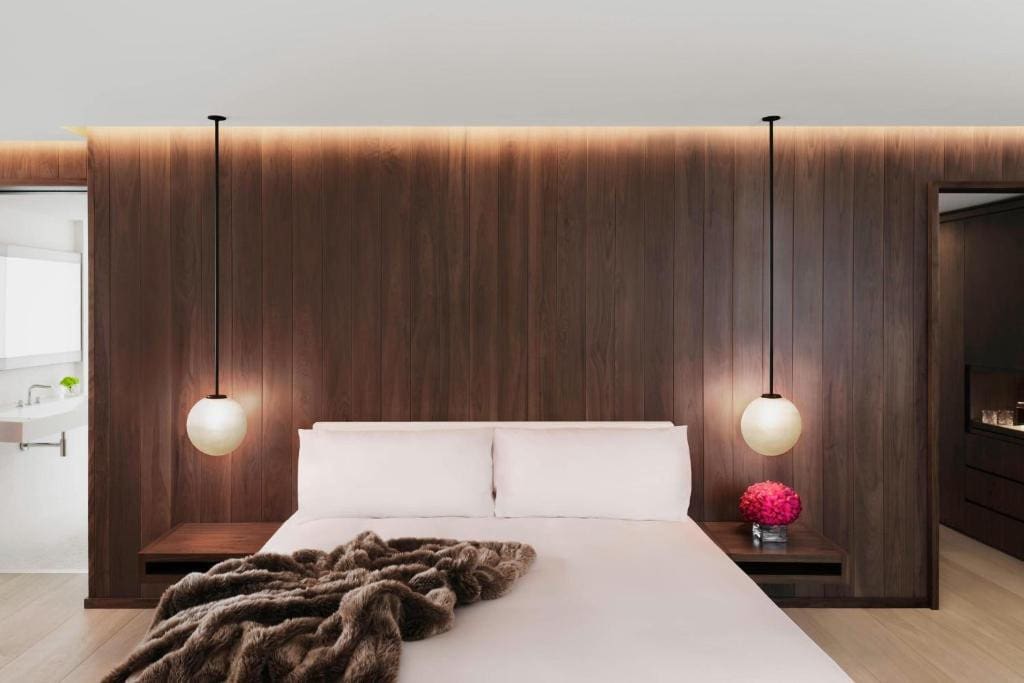 27 Best London Hotels with Balconies 2024 10 A bedroom with wooden walls and a bed. A bed with brown thich blanket can be seen with bedside tables on eachh side. This is the London Edition one of the best london hotels with balconies.