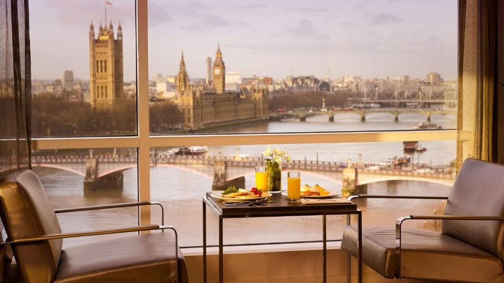 27 Best London Hotels with Balconies 2024 14 A square table and chairs for two with a breakfast set-up beside a large window with a view of a bridge and a large clock tower. This is the Park Plaza London Riverbank.