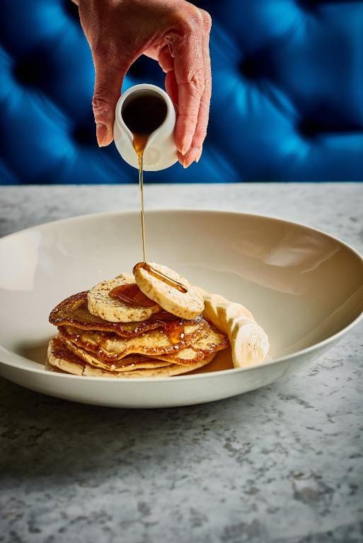 27 Best London Hotels with Balconies 2024 20 A person pouring syrup on a plate of pancakes. Get a taste of wonderful cuisine at the Apex City of London Hotel.
