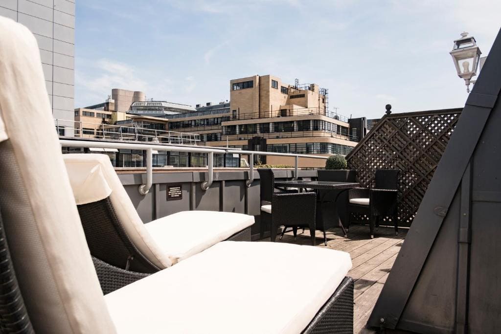 27 Best London Hotels with Balconies 2024 23 A balcony with rattan furniture, woden floorings, and concrete railings with a vew of lage buildings in the city. This is in the Chamberlain, London.